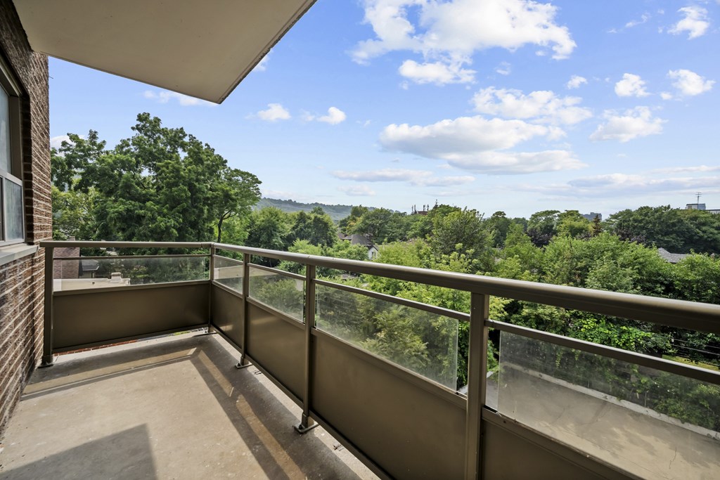 A balcony with a metal railing overlooks a lush green landscape.