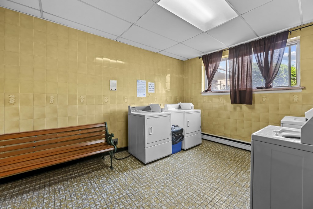 A room with a bench, a window with curtains, and a washing machine.
