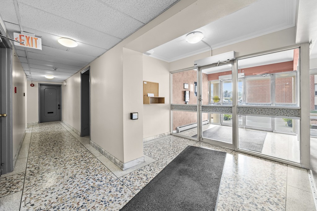 A hallway with a tiled floor and a black and white runner leading to a door.