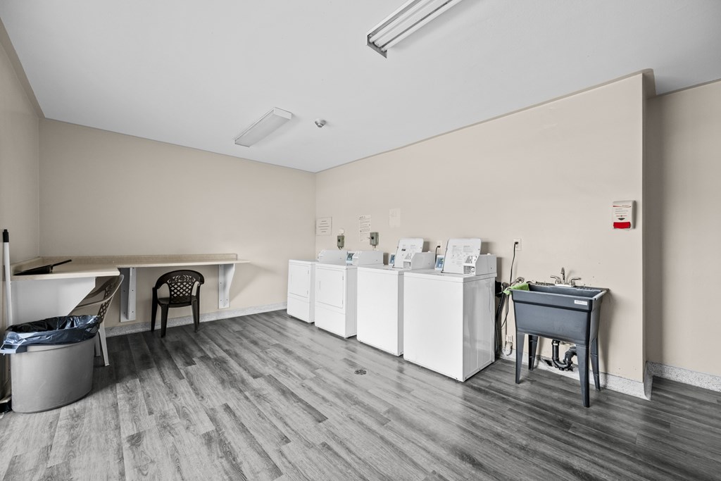 A room with a white table, a black chair, and a grey trash can.