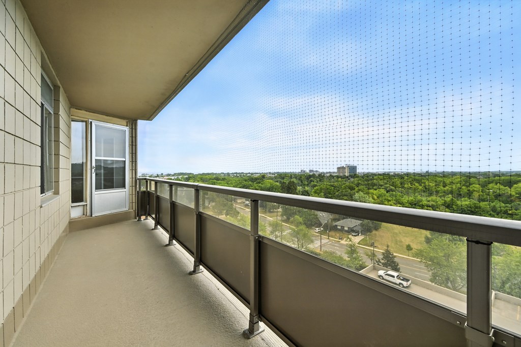 A balcony with a view of a parking lot and trees.