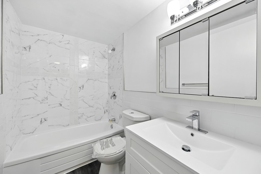A white bathroom with a marble wall and a toilet paper roll.