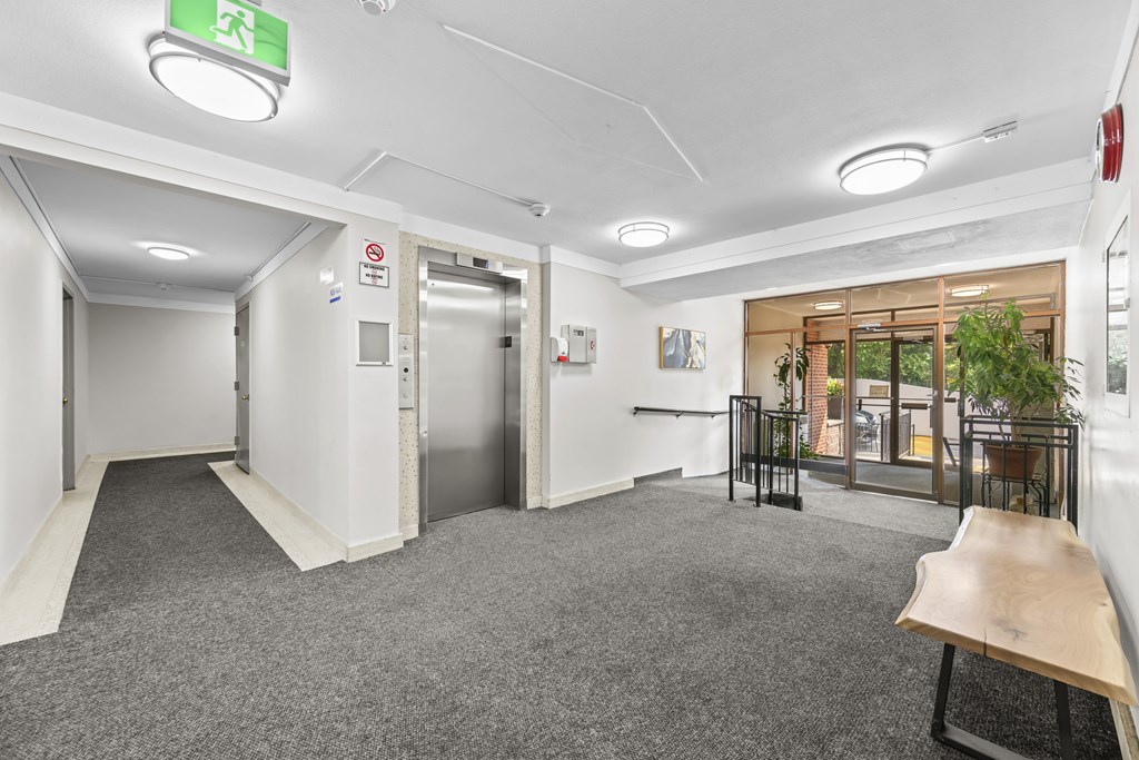A hallway with a green exit sign and a bench.