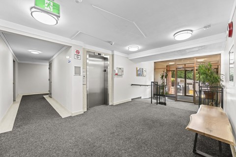 A hallway with a green exit sign and a bench.