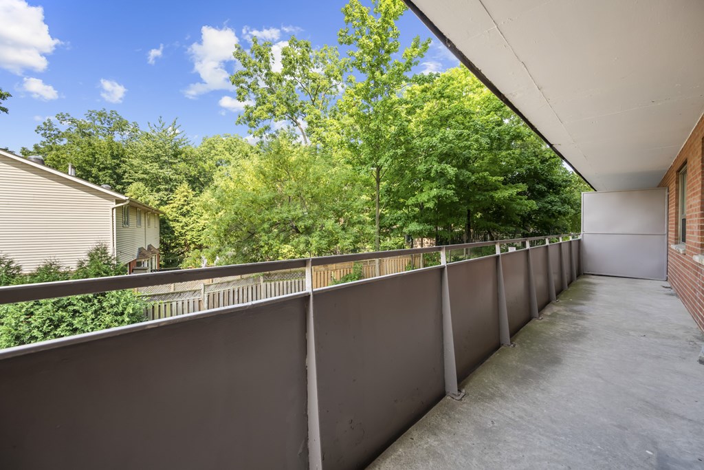 A long concrete balcony with a grey railing and trees in the background.