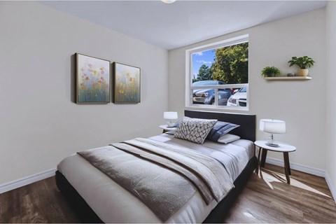A bedroom with a bed, a nightstand, and a window with a view of a parking lot.