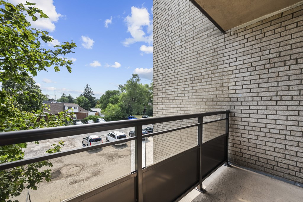 A balcony with a metal railing overlooks a parking lot and trees.