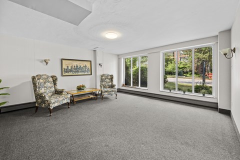 A living room with a grey carpet and a painting on the wall.