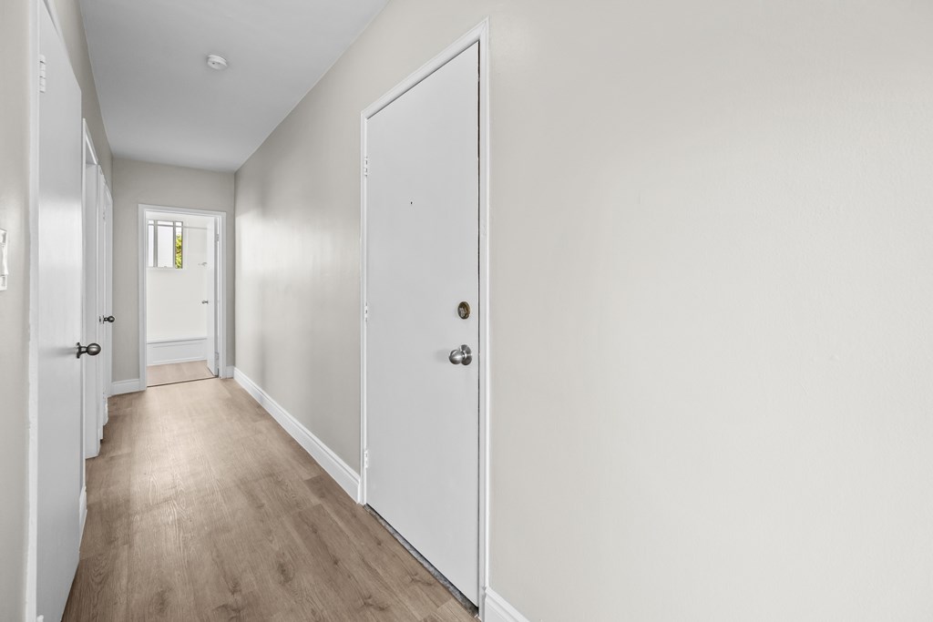 A long white hallway with a white door on the right.
