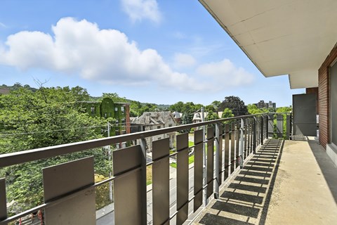 A balcony with metal railings overlooks a lush green landscape.