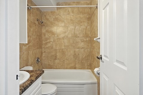 A bathroom with a beige tile shower and white fixtures.