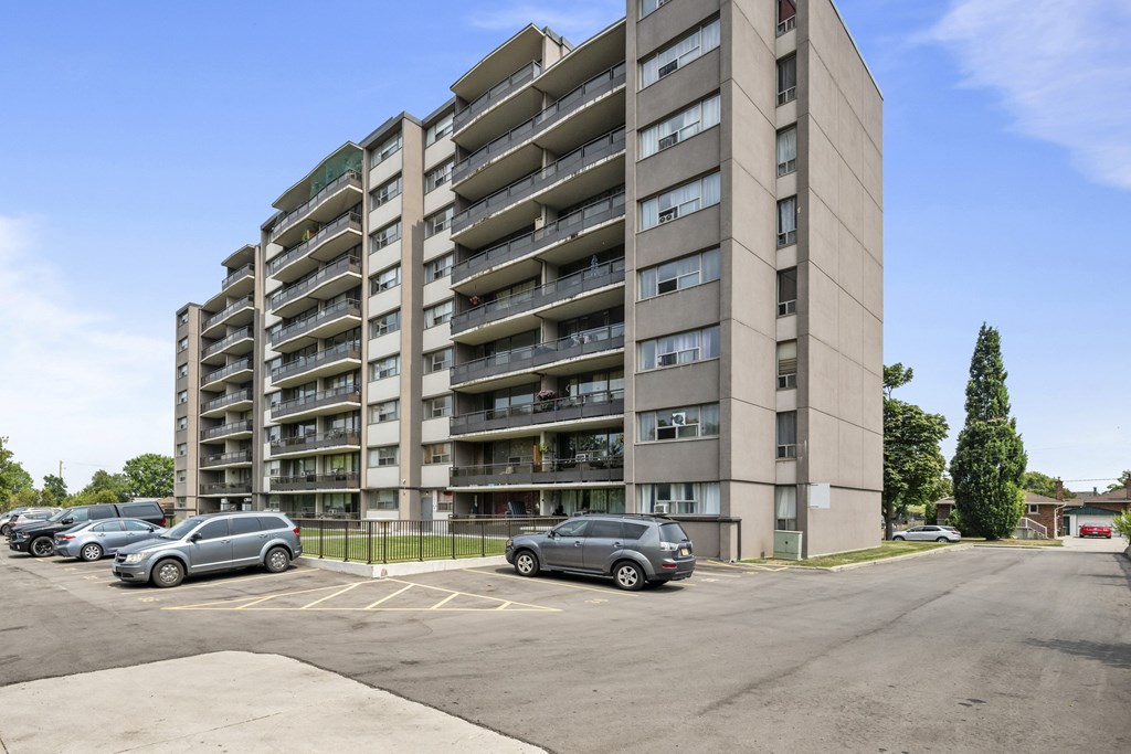 A tall apartment building with a parking lot in front.