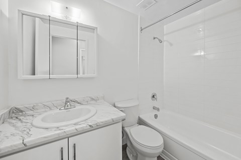 A white bathroom with a marble countertop and a toilet.