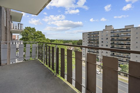 A balcony with a metal railing overlooks a road and buildings.