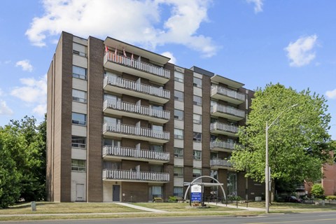 A tall apartment building with balconies and a blue sign in front.