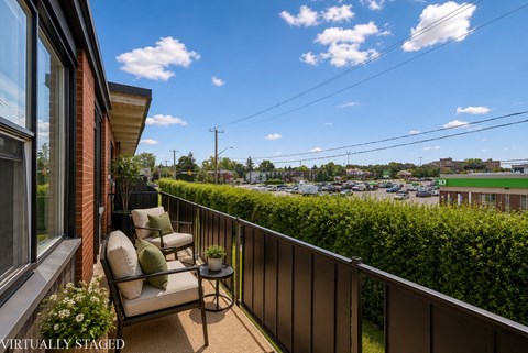 A balcony with a chair and table overlooking a parking lot.