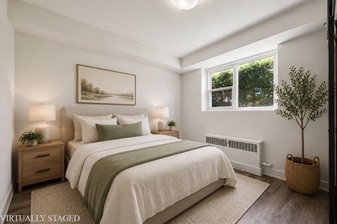 A bedroom with a large bed, a small tree, and a painting on the wall.
