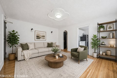 A living room with a white couch, a green armchair, a wooden coffee table, and a white rug.