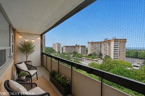 A balcony with a chair and a table overlooking a cityscape.