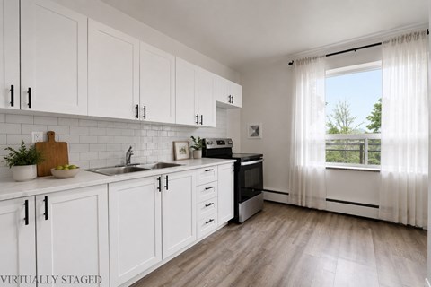 A kitchen with white cabinets and a wooden cutting board.