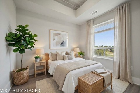 A bedroom with a large bed, a plant, and a window with curtains.