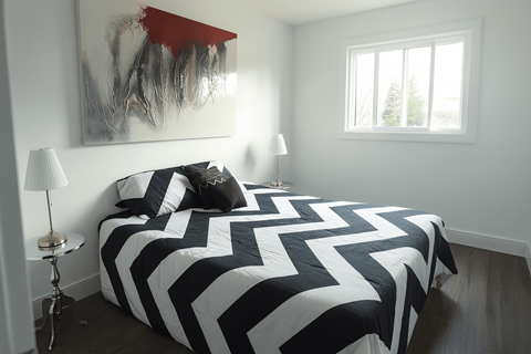 A bed with a black and white striped comforter sits in a room with a painting on the wall and a window.