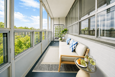 A white couch with a blue and white pillow is in front of a window with a view of trees.