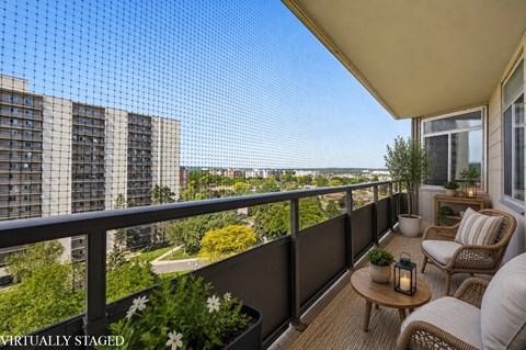 A balcony with a table, chairs, and a lantern with a view of a city in the background.