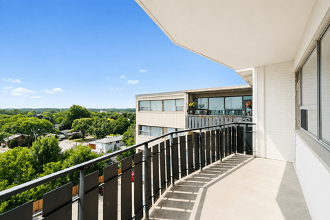 A balcony with a metal railing and steps leading to a building with a glass door.