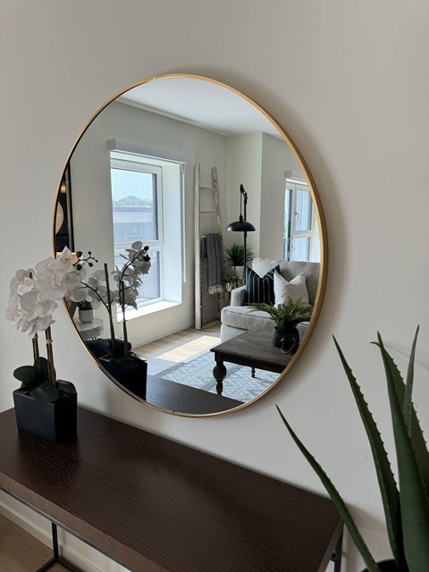 A round mirror with a gold frame reflects a living room with a white couch and a black coffee table.