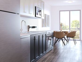 A modern kitchen with dark grey cabinets and a wooden floor.at The Maverick, Kitchener