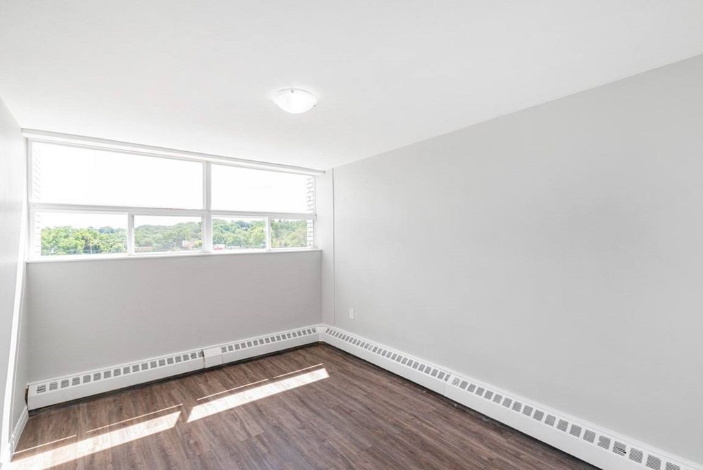 A room with white walls and a window with a view of trees outside.