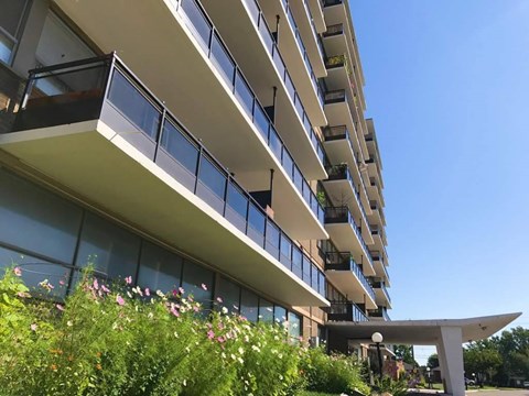 A modern building with balconies and plants in front.
