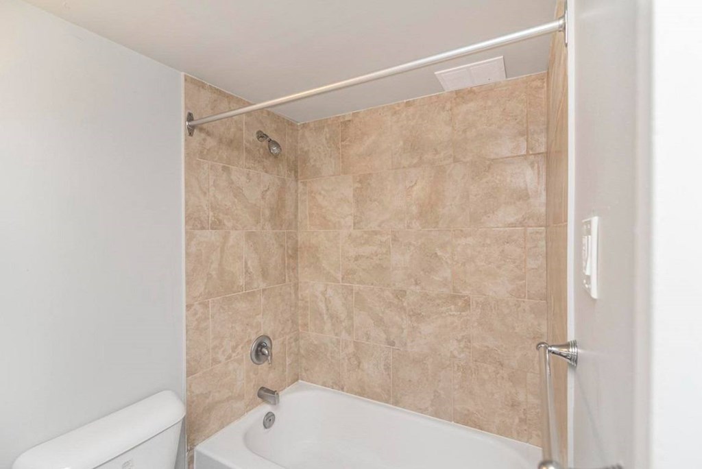 A bathroom with a white tub and beige tiled walls.