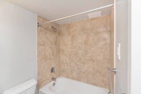 A bathroom with a white tub and beige tiled walls.