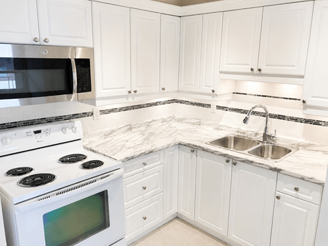 A white kitchen with a stove, microwave, and sink.