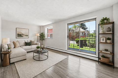 A living room with a white couch, a coffee table, and a large window with a view of a backyard.