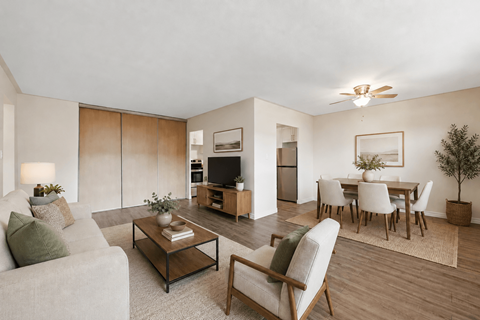 A living room with a grey couch, a coffee table, a chair, a potted plant, and a dining table set up.