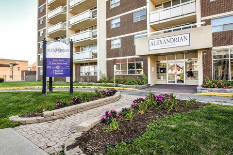 The entrance to the Alexandrian apartment complex is shown with a sign and flower bed in front.