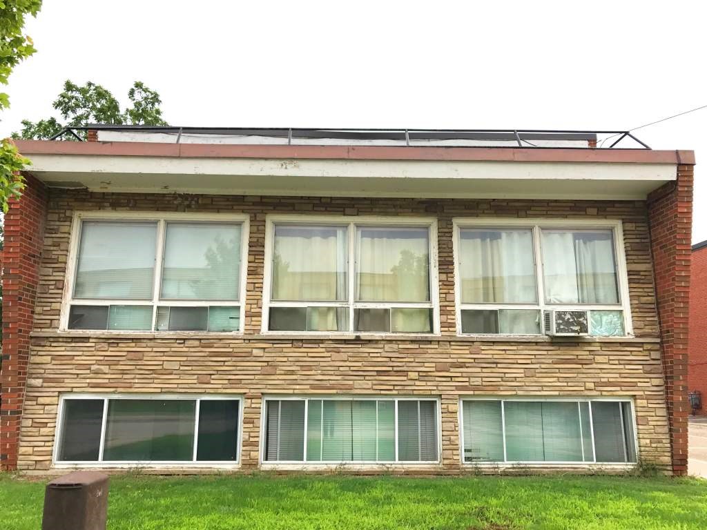 A brick house with a red roof and white curtains on the windows.