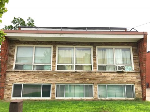 A brick house with a red roof and white curtains on the windows.