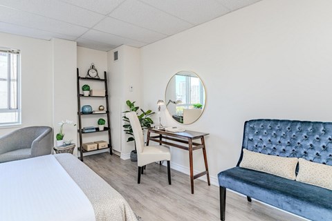 A bedroom with a bed, a chair, a desk, and a mirror.