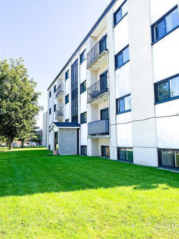 A white building with balconies and a green lawn in front.