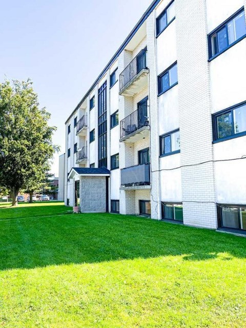 A white building with balconies and a green lawn in front.