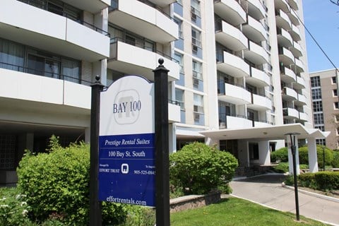 A sign for Bay 100 Apartments stands in front of a white building.