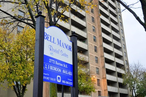 A sign for Bell Manor Rental Suites is displayed in front of a tall building.