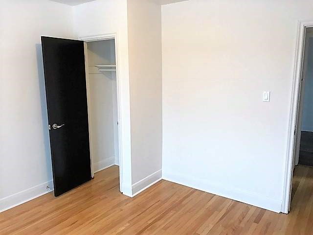 A black wardrobe stands in a room with a white wall and wooden floor.