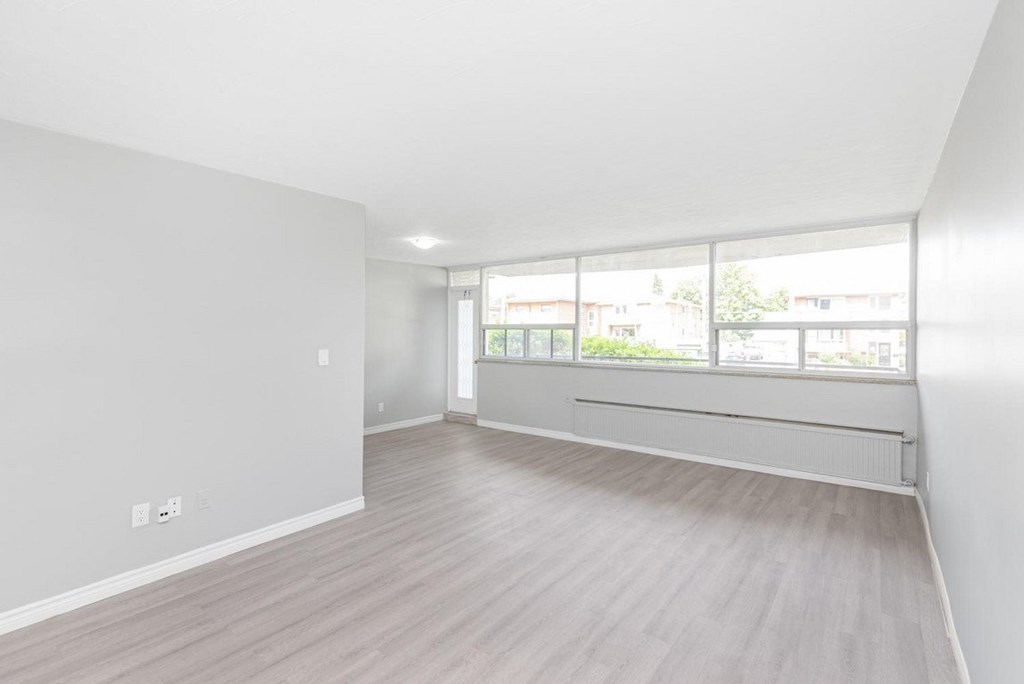 A spacious room with light wood flooring and large windows.