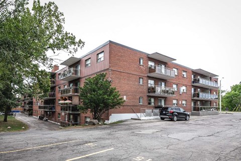 A black car is parked in front of a red brick apartment building.