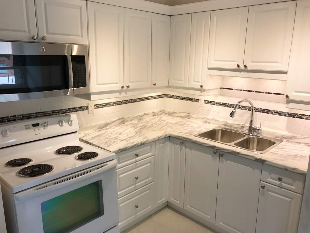 A kitchen with white cabinets and a marble countertop.